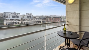 A balcony with a table and chairs, overlooking a river and buildings. - The Tygervalley Escape (Cape Town)