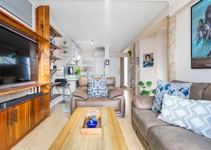A modern living room with a large flat-screen TV, wooden cabinets, a leather sofa, and a coffee table. - The Tygervalley Escape (Cape Town)