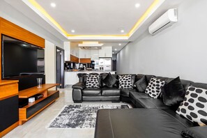 A modern living room with a black leather sofa, wooden entertainment unit, and a flat-screen TV. - Sairia House (La Mercy)