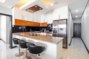 A modern kitchen with a central island, black bar stools, stainless steel appliances, and a wooden accent wall.