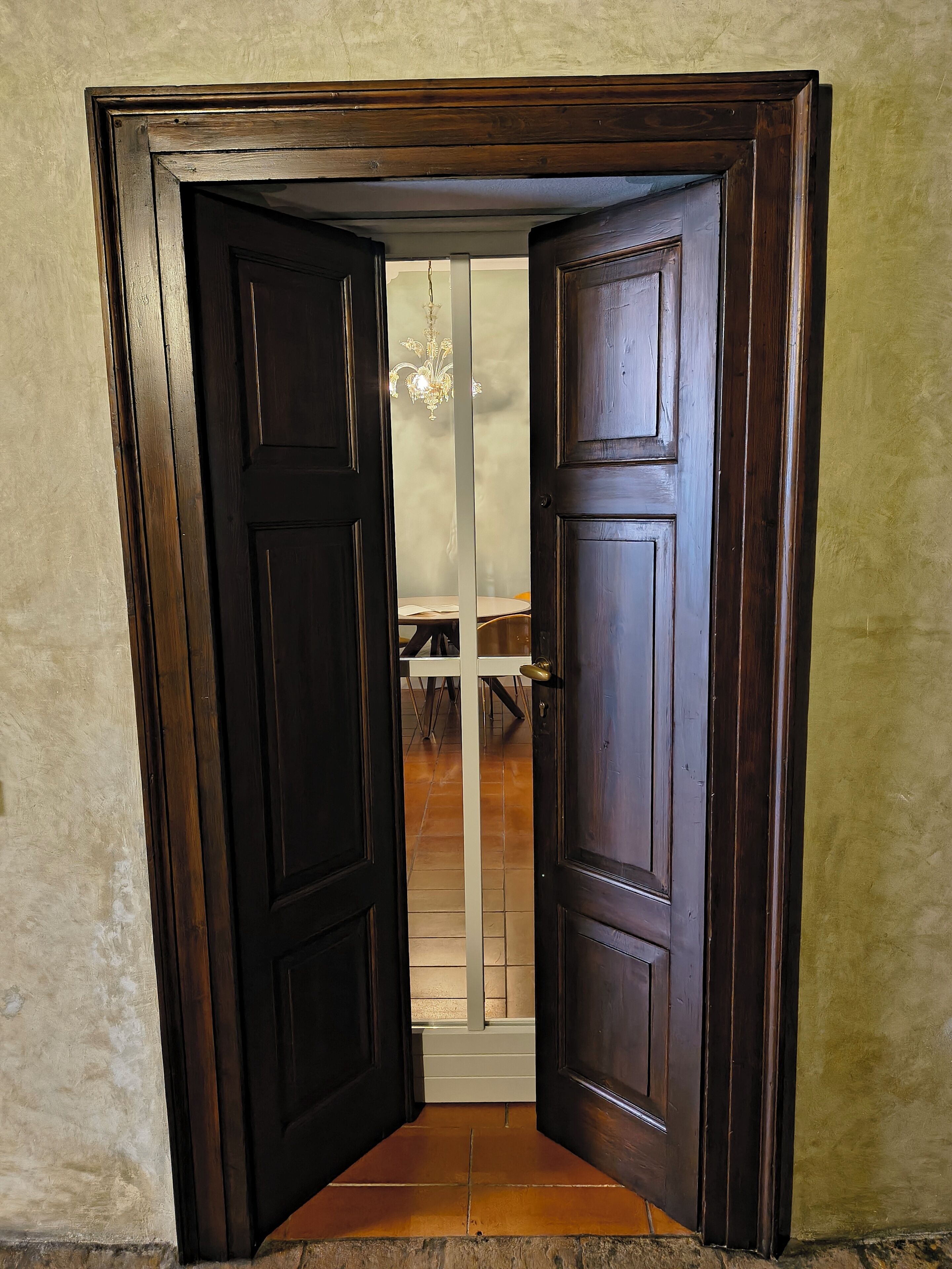 A dark wooden door with a white frame, leading to a room with a tiled floor and a chandelier.
