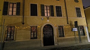 Ein zweistöckiges Gebäude mit einer mittleren Eingangstür, zahlreichen Fenstern mit Fensterläden und einem Schild, das auf ein Geschäft oder Unternehmen hinweist.