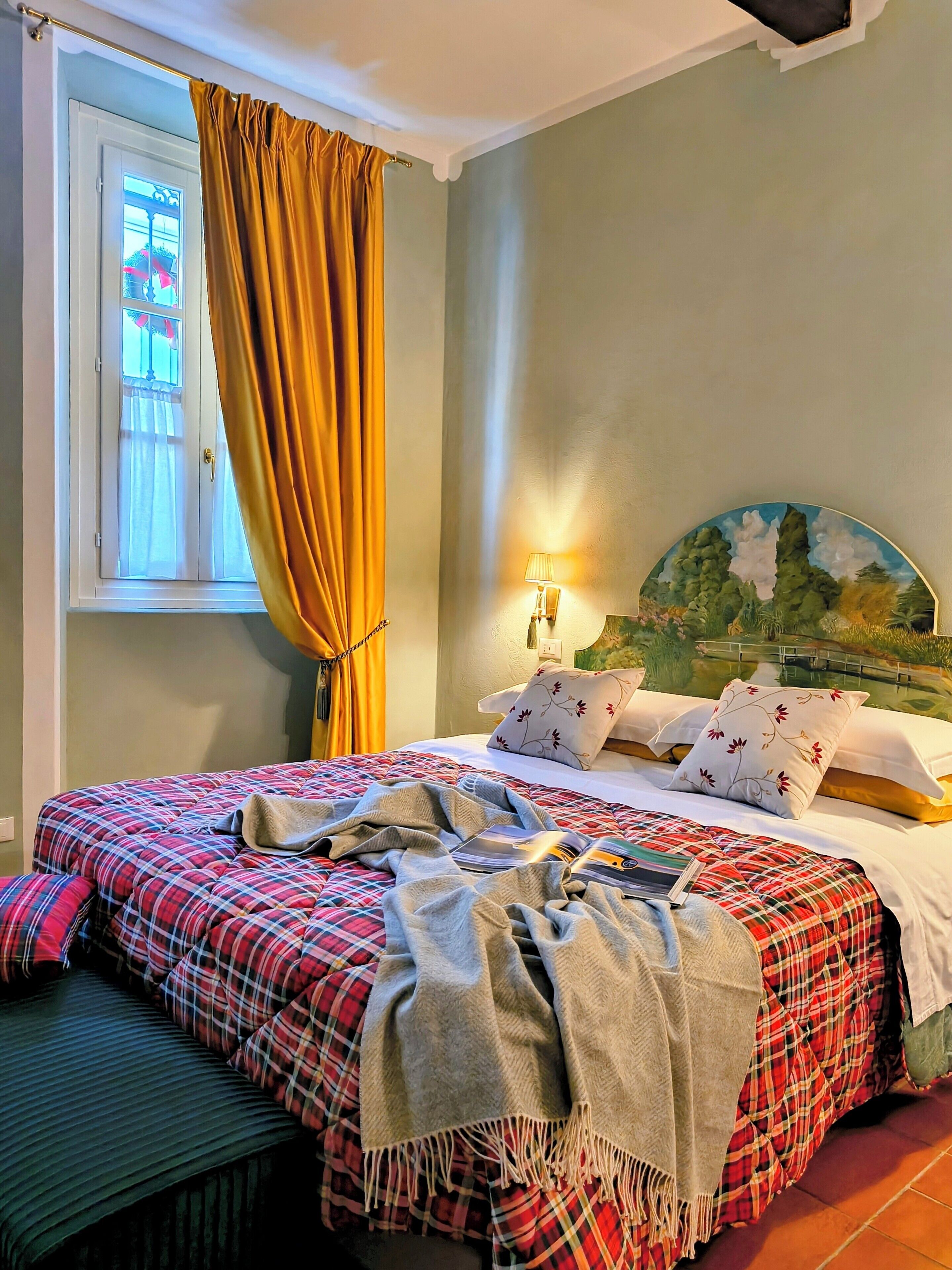 Una camera da letto con un letto, una finestra con tende, una lampada a parete e un quadro.