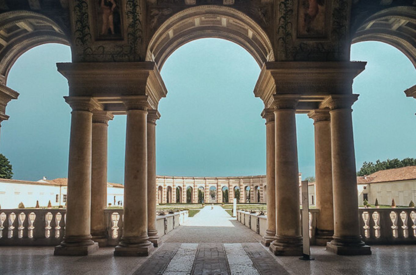 A grand architectural structure with a central pathway flanked by large columns and arches, leading to a distant building.
