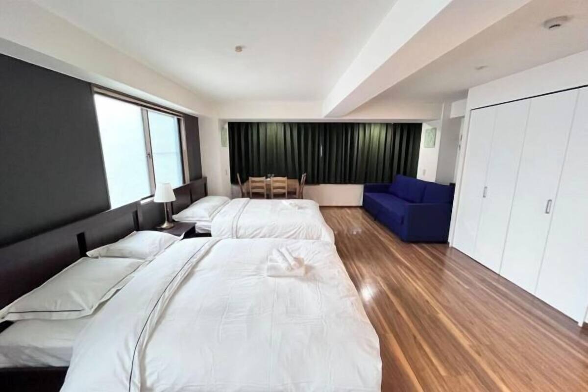 A hotel room with two beds, a blue sofa, a dining table, and a wardrobe.