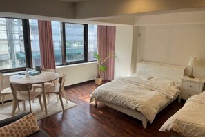 A hotel room with a bed, bedside table, lamp, window with curtains, a small table with chairs, and a potted plant. - Iorishimodera (Osaka)
