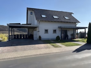 Une maison moderne à deux étages, dotée d’une allée couverte, d’un petit jardin et offrant une vue sur le paysage environnant.