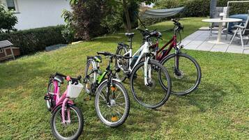 Des vélos sont garés sur une pelouse verdoyante, un bâtiment blanc se dresse à proximité, et un hamac est visible au fond.