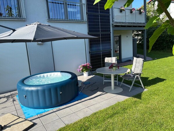 Un jardin avec un jacuzzi, une table et des chaises, et un parasol de patio.