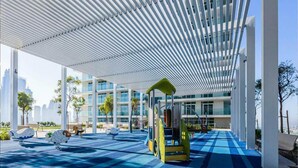 Zona de juegos al aire libre con piso a cuadros azules, un juguete amarillo para montar y una estructura de toldo blanco.