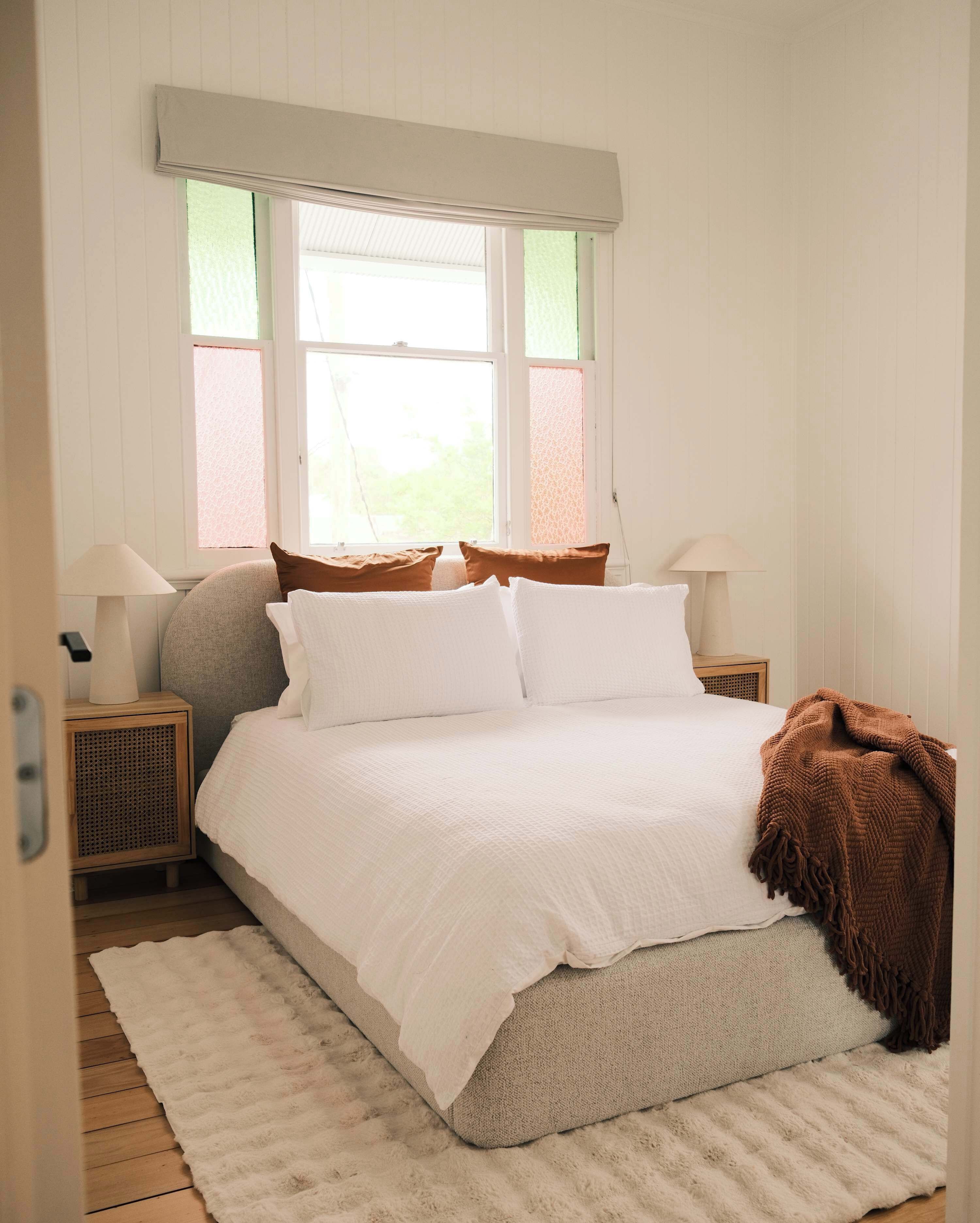 Un dormitorio con cama, dos mesitas de noche, una ventana con persianas y una puerta.