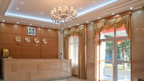 A hotel reception area with a marble counter, a chandelier, and large windows with curtains. - Fude Hotel (Tbilisi)