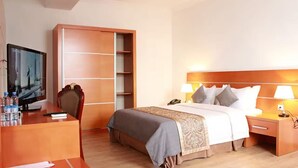 A hotel room with a bed, bedside table, lamp, desk with computer and water bottles, and a TV. - Fude Hotel (Tbilisi)