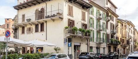 A street with parked cars and a building with balconies and shutters.