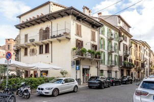Una calle con coches aparcados y un edificio con balcones y contraventanas.