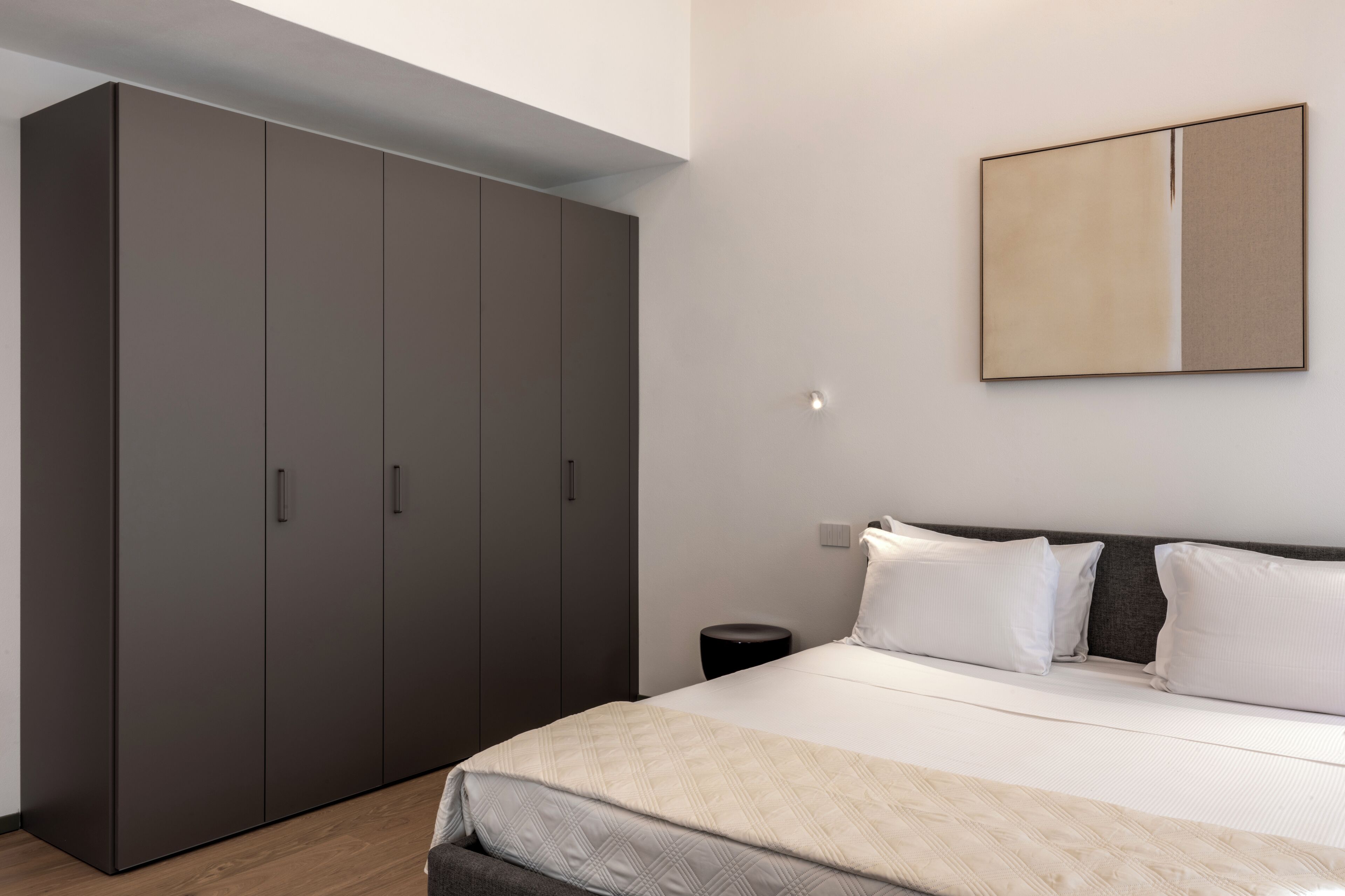 A bedroom with a bed, a wardrobe, and a wall-mounted artwork.