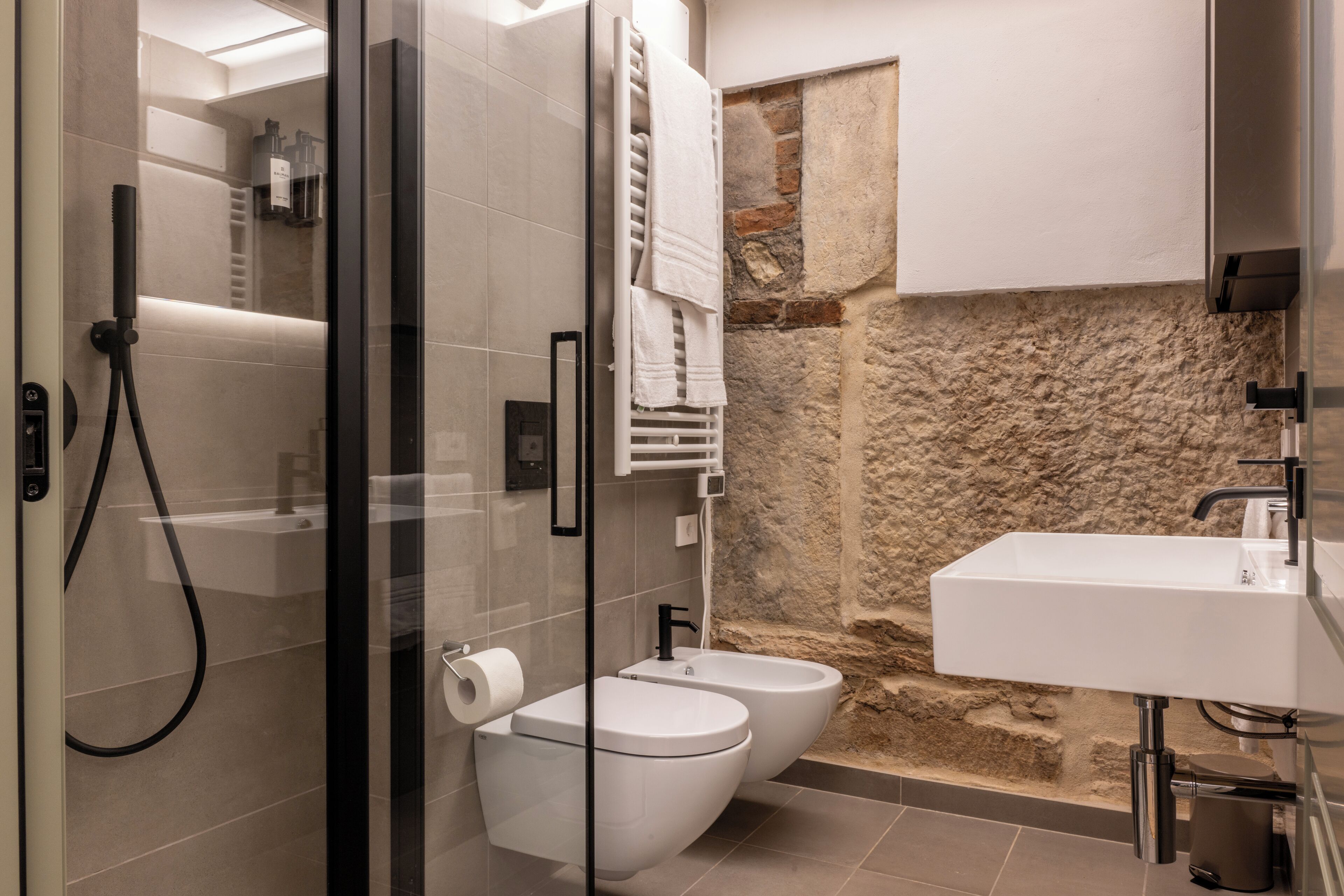 A modern bathroom with a glass-enclosed shower, a white sink, and a stone accent wall.