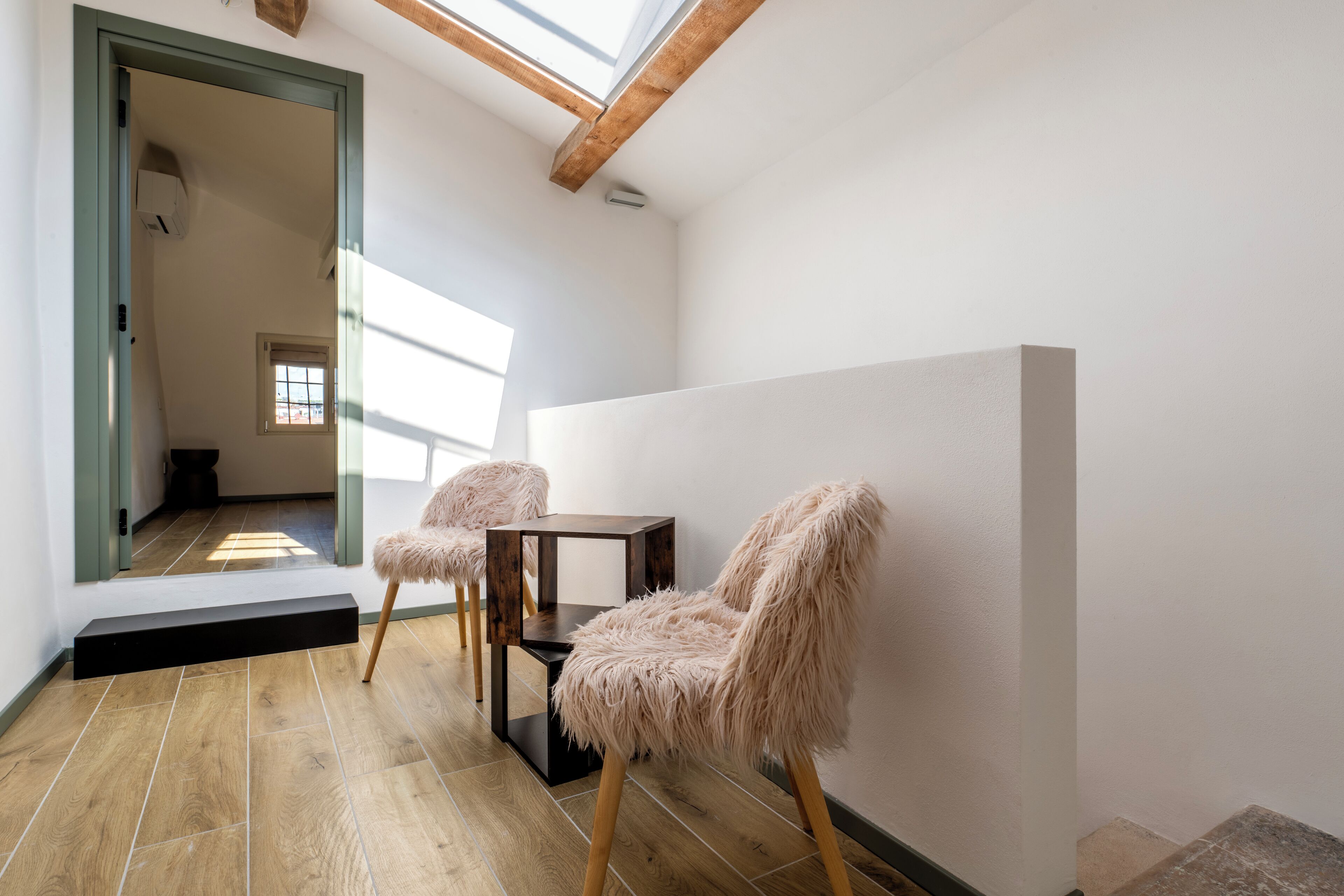 A modern room with a skylight, wooden flooring, and two fluffy chairs by a small table.