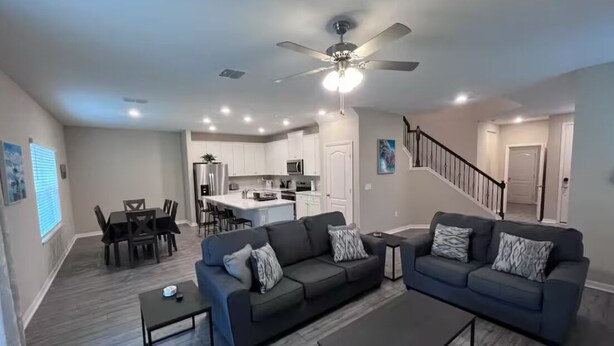 A modern living room with two dark sofas, a coffee table, and a dining area with a table and chairs. A kitchen is visible in the background, and a staircase leads to another level. - Relax near Historic St. Augustine & Beaches (St. Augustine)