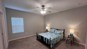 A bedroom with a bed, ceiling fan, two bedside lamps, and a window with blinds. - Relax near Historic St. Augustine & Beaches (St. Augustine)