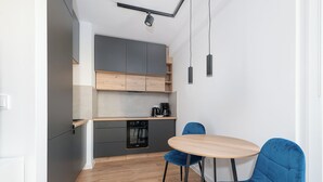 Une cuisine moderne avec des meubles gris, un lave-vaisselle et une machine à café. On y trouve une table ronde en bois, accompagnée de deux chaises bleues.