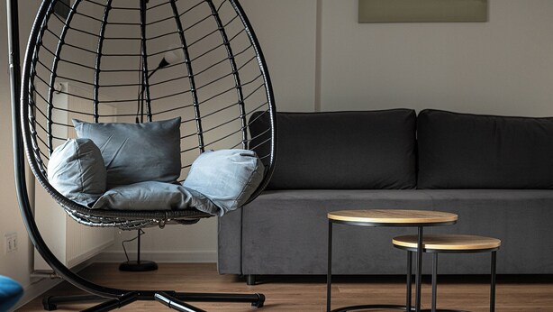 Un salon moderne avec un canapé gris, un fauteuil suspendu noir agrémenté de coussins et une petite table en bois.