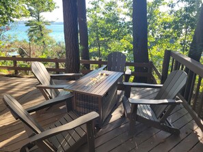 Une terrasse en bois avec des fauteuils Adirondack et une table autour d’un foyer.