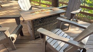 Une terrasse en bois avec des fauteuils Adirondack, un foyer et une table.