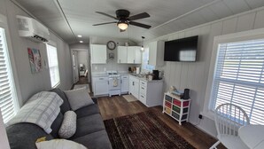 A compact living space with a kitchenette, a dining area, and a seating area with a sofa and a chair. - Little Barnstead Tiny Home (Big Cabin)