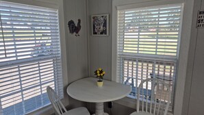 A small room with a round white table and two white chairs, a single yellow flower in a pot, and a rooster decoration on the wall. - Little Barnstead Tiny Home (Big Cabin)