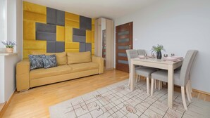 Una sala moderna con un sofá amarillo, una mesa de comedor con sillas y un panel de pared geométrico.