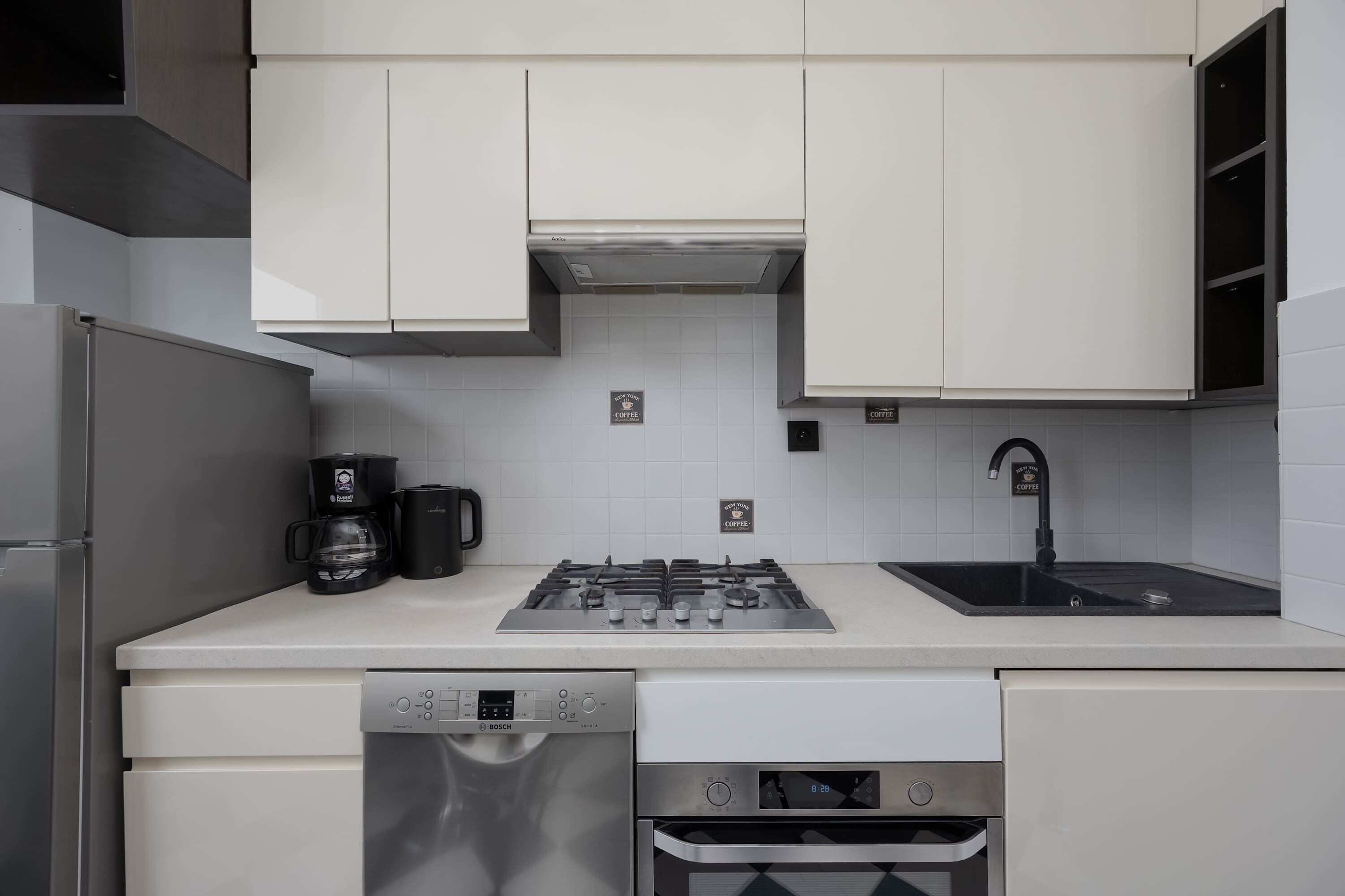 A modern kitchen with white cabinetry, a Bosch dishwasher, a gas stove, and a coffee maker.
