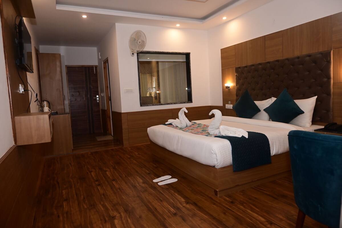 A hotel room with a wooden floor, a large bed with white bedding, a blue chair, a wooden wardrobe, and a window with curtains.