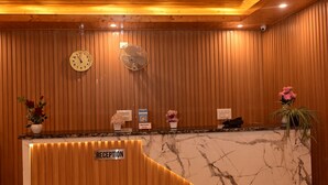 Un mostrador de recepción con detalles de madera y mármol, un reloj y un ventilador en la pared.