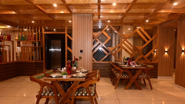 A dining area with wooden tables and chairs, a bar with bottles, and a large pillar. - Mystic  Manali (Manali)