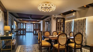 A spacious dining area with a patterned rug, wooden chairs, and a chandelier. - Azydo, Art House, Grand Road, Near Jagannath Mandir (Puri)