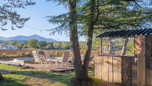 Een houten terras met lounge fauteuils, een jacuzzi en een klein houten bouwwerk met dak.
