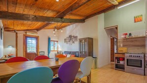 A dining area with a wooden table and colorful chairs, a kitchen with a stove and cabinets, and a living area with a sofa and a window.