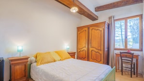 A bedroom with a bed, wooden wardrobe, desk, chair, and a window with curtains.
