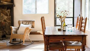 A dining area with a wooden table, wicker chairs, and a vase with dried flowers. - Treehouse Retreat | Sleeps 10 | Big Deck (Shaver Lake)