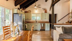 A modern kitchen with light-colored cabinets, a wooden dining table with chairs, and a staircase leading to an upper level. - Treehouse Retreat | Sleeps 10 | Big Deck (Shaver Lake)