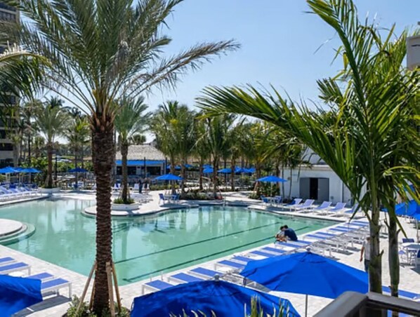 A pool area with lounge chairs and umbrellas, surrounded by palm trees.