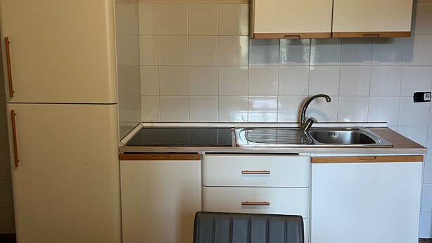 A compact kitchen with a white refrigerator, a sink, and a small dining area. - two-room apartment, mirabilandia (Fosso Ghiaia)