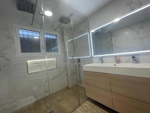 Een moderne badkamer met een glazen douchecabine, een grote spiegel en een wit wastafelmeubel met een houten kastje.