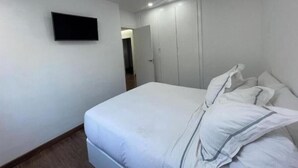 Un dormitorio con una cama, un televisor de pantalla plana montado en la pared y un armario.