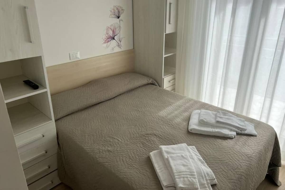A bedroom with a bed, a wardrobe, and a painting of flowers on the wall.