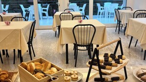 Un'area ristorazione con tavoli e sedie, un buffet con dolci, e ampie finestre vista su spazi verdi.