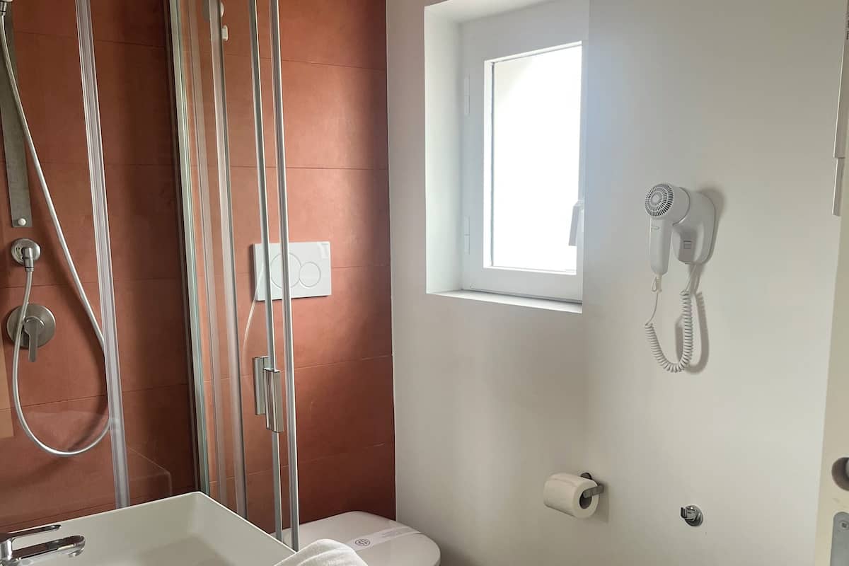 A bathroom with a shower, toilet, bidet, and a small window.