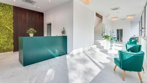 Un'accoglienza moderna con una reception verde, un giardino verticale e una scala che conduce ai piani superiori.
