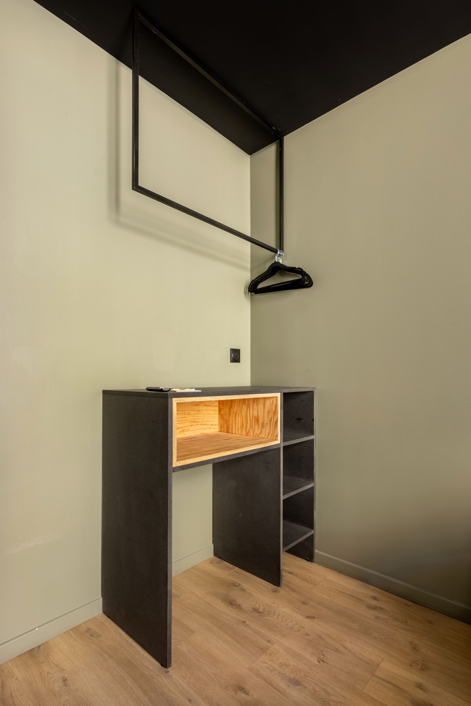 Une pièce moderne avec un bureau sombre, une étagère en bois et un luminaire suspendu.